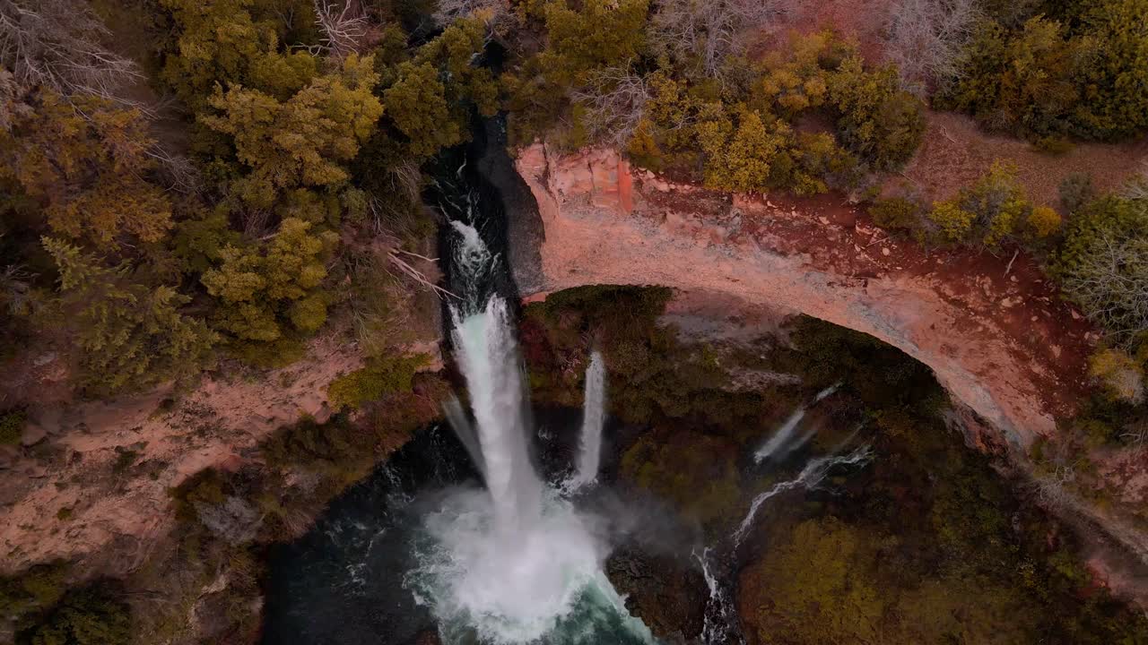 Top-down bird's eye drone view of waterfall with mist into turquoise pool, Siete Tazas National Park, Ñuble, Chile with red rock cliffs