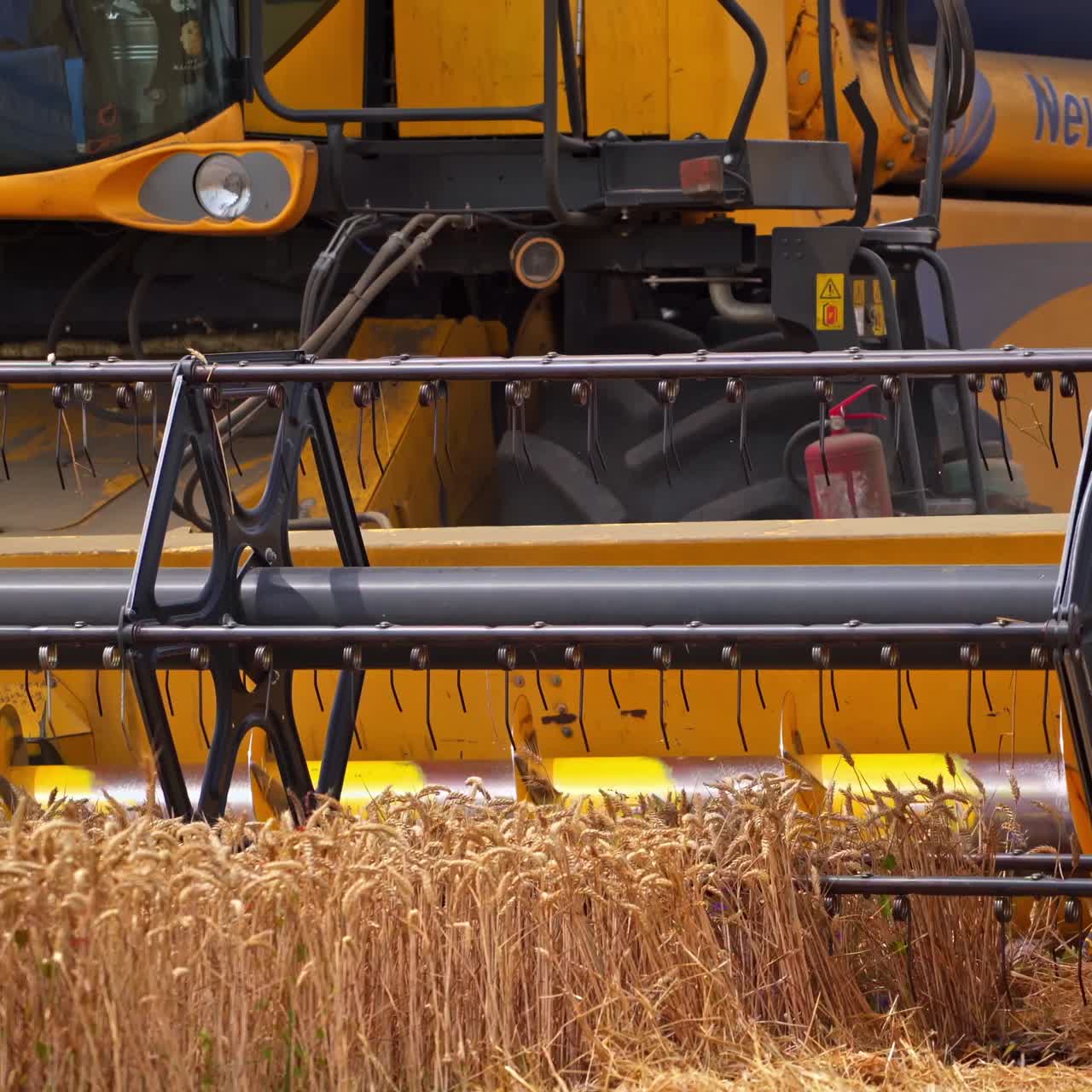 Huge mowing machine cuts the ripe wheat spikelets. Big yellow combine harvester approaching the camera. Spinning mowing mechanism close up