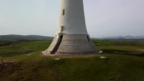 Aerial-spinning-shot-around-the-base-of-Sir-John-Barrow-Monument,-highlighting-its-detailed-stonework-and-serene-landscape