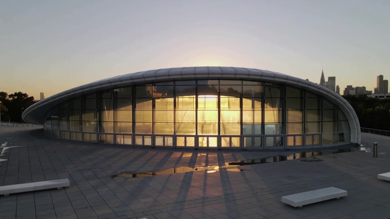 Sol poniente bañando una cúpula de cristal curvado en una terraza en la azotea con bancos y charcos