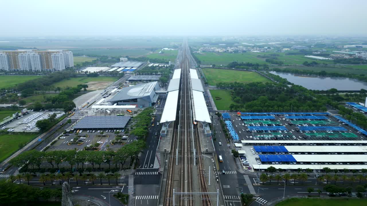 Aerial birds eye shot of Chiayi City Taiwan HSR Train Station with cars on street. Cloudy day with fog in Asia. Agricultural farm fields in rural area.