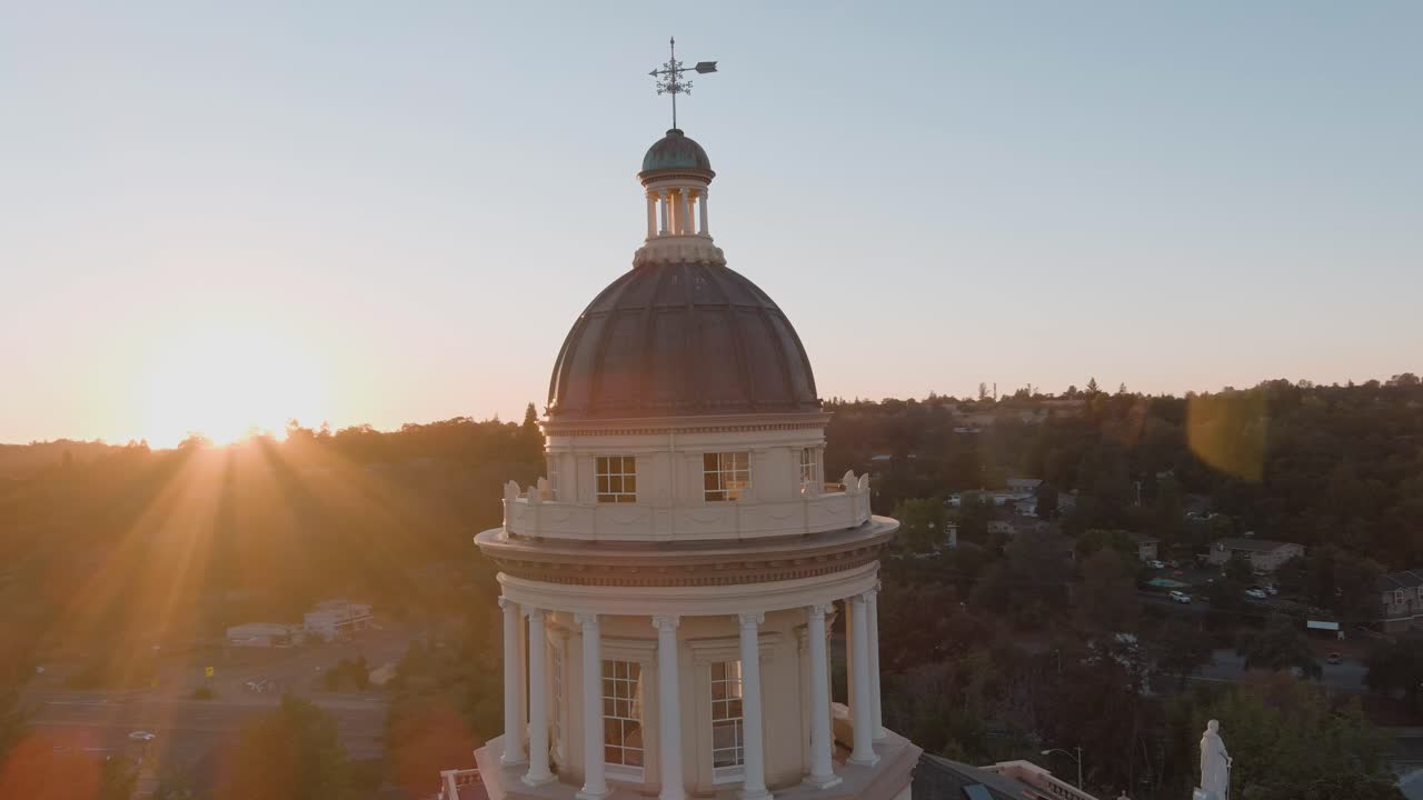 Drone orbit around Auburn Courthouse dome at sunset, with sun rays crossing the building and city in the background