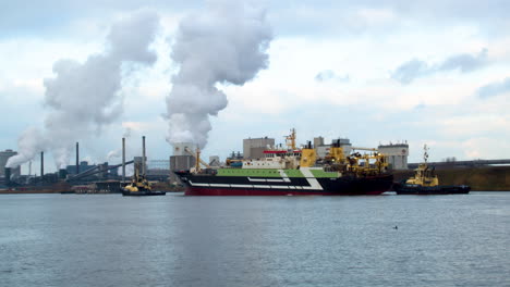 Barco-Grande-Guiado-Al-Puerto-Por-Remolcadores-Con-Industria-Contaminante-En-El-Fondo---Medio