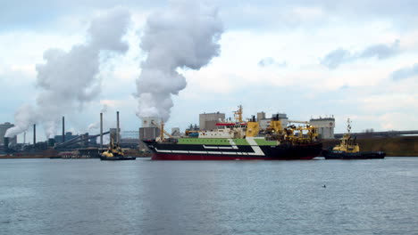 barco grande guiado al puerto por remolcadores con industria contaminante en el fondo - medio