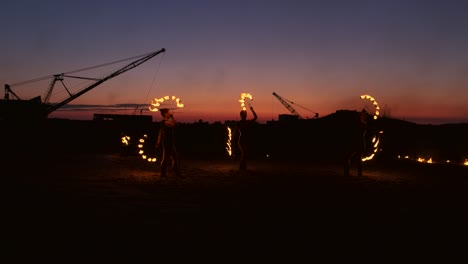 professional artists show a fire show at a summer festival on the sand in slow motion. fourth person acrobats from circus work with fire at night on the beach.