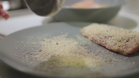 chef rociando semillas de amapola y sésamo en un plato para pescado salmón