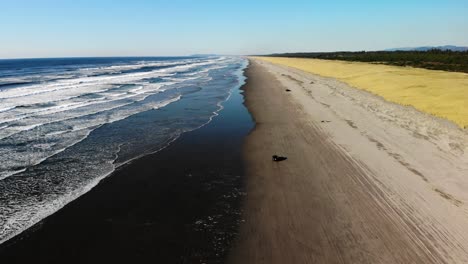 Isoliertes-Auto,-Das-Allein-über-Sandstrand-In-Der-Nähe-Von-Ozeanwasser-Mit-Großen-Wellen-Fährt