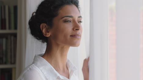 hermosa mujer de raza mixta mirando por la ventana en casa disfrutando de un nuevo día fresco sintiéndose descansada pensando en planear por delante imágenes de 4k