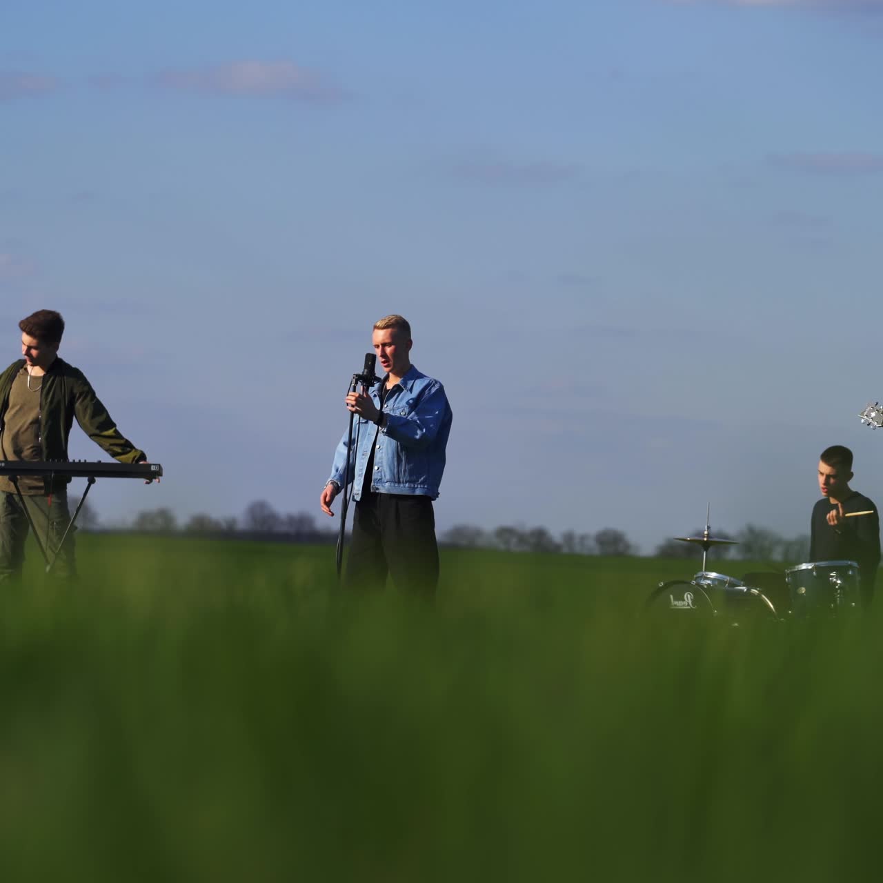 Young men gathered in music band to perform rock music. Male musicians play diverse instruments, sing and dance in the farmlands. Blurred foreground