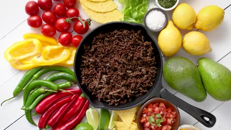 ingredientes para chili con carne en una sartén de hierro sobre una mesa de madera blanca