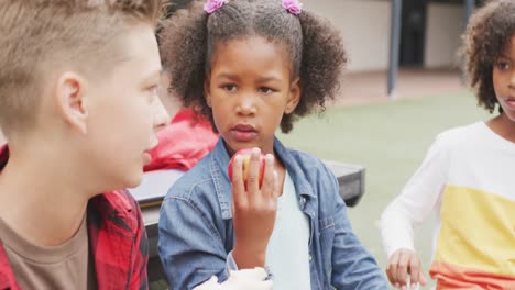 video de tres escolares diversos comiendo almuerzos envasados, hablando en el patio de la escuela