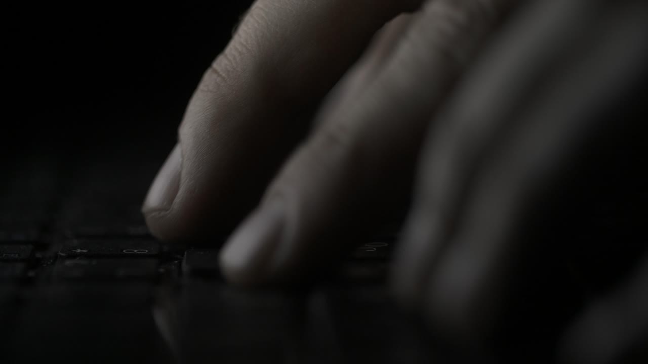 Close-up of hands typing on a laptop keyboard at night