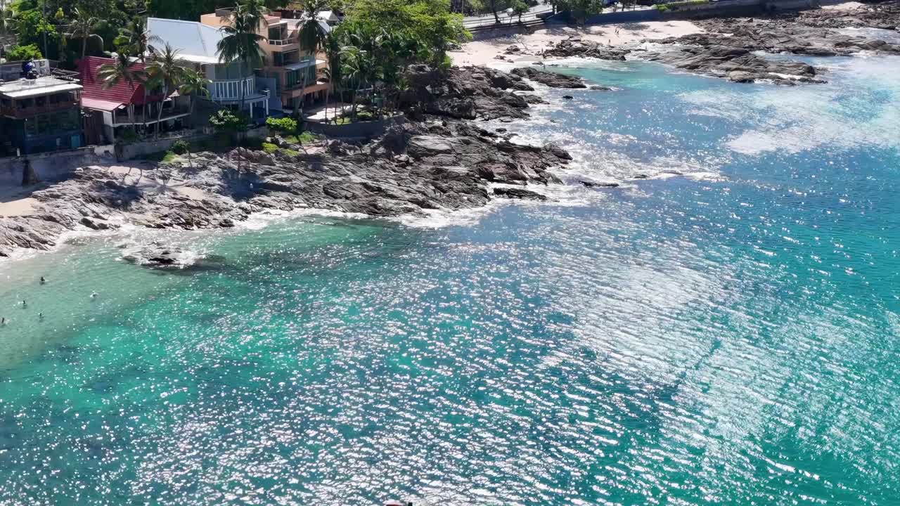 Drone footage captures Phuket's vibrant coastline, showcasing turquoise waters, rocky shores, and lush greenery under bright daylight