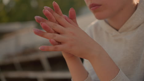 close-up of woman with hands gently locked together, well-polished nails in focus, expressing a thoughtful and introspective mood, sunlight softly illuminates her