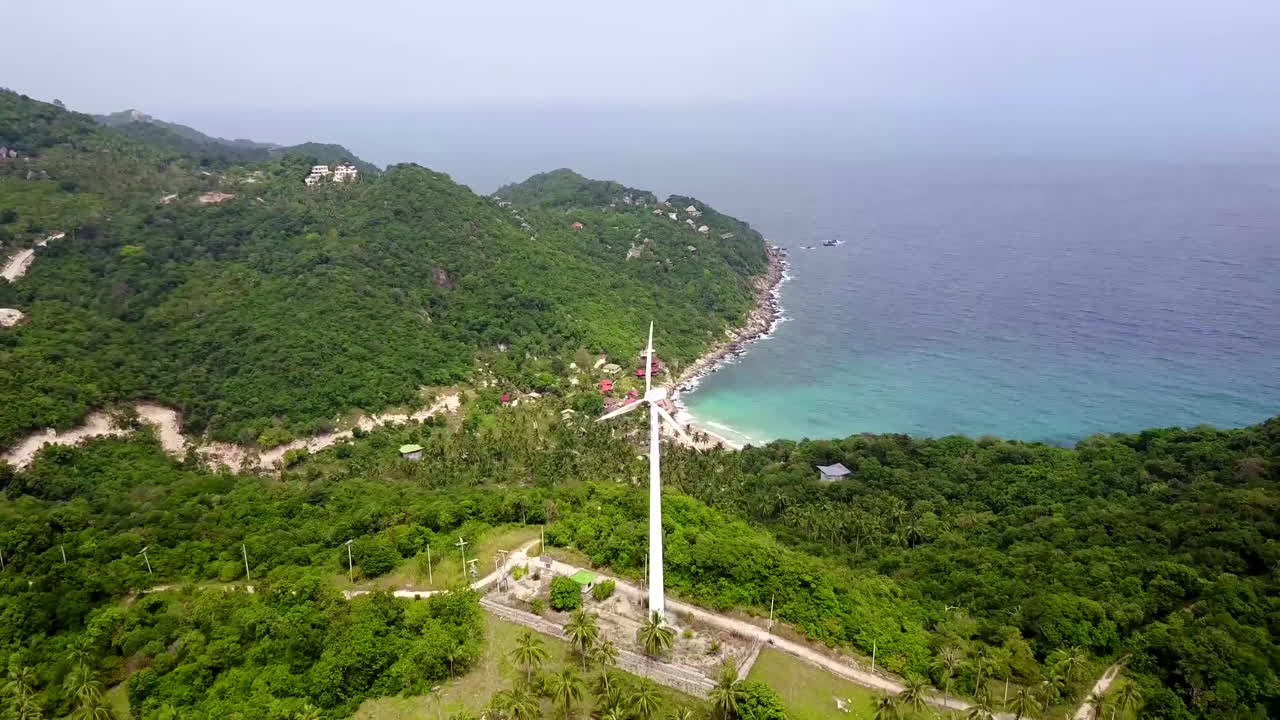 Aerial view at tropical island and the sea. Camera moves forward flies next to a wind generator. Bright sunny day. Koh Tao. Thailand