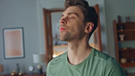 healthy man drinking water from glass bottle in apartment living room close up