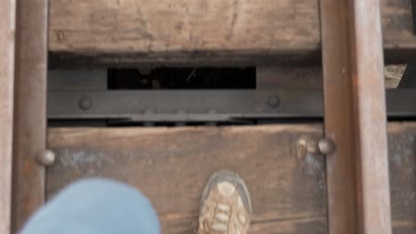 man walks over train trestle while looking down into ravine through railway rails and ties