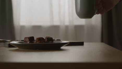 cerca de una persona comiendo brownies de chocolate y bebiendo bebida caliente de la taza