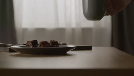 close up of person eating chocolate brownies and drinking hot drink from mug