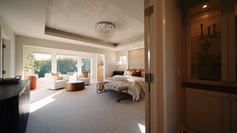 a luxurious bedroom with a large bed, cozy seating area, and chandelier, filled with natural light from multiple windows.