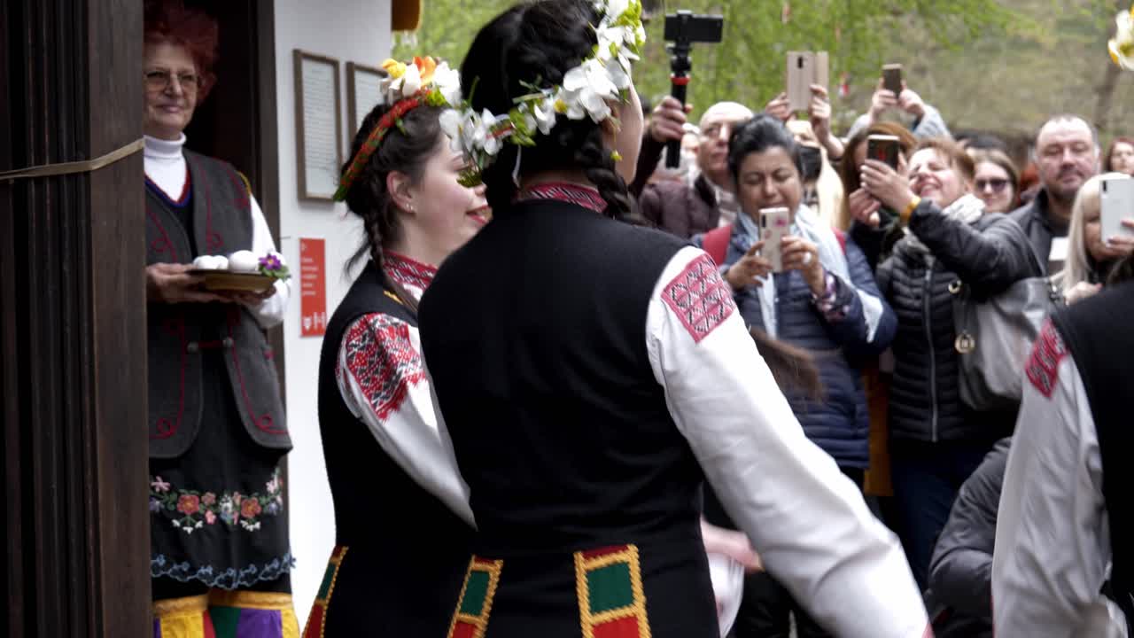 Pretty, Bulgarian girls in colourful traditional dress perform Easter time ritual dance in front of crowds Slow mo.