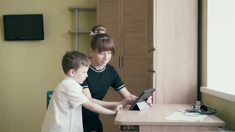 seguimiento joven madre bonita muestra a su hijo cómo hacer la tarea utiliza una tableta