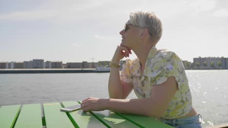 una linda joven turista observa los barcos en la bahía, sentada a la luz del sol en un muelle