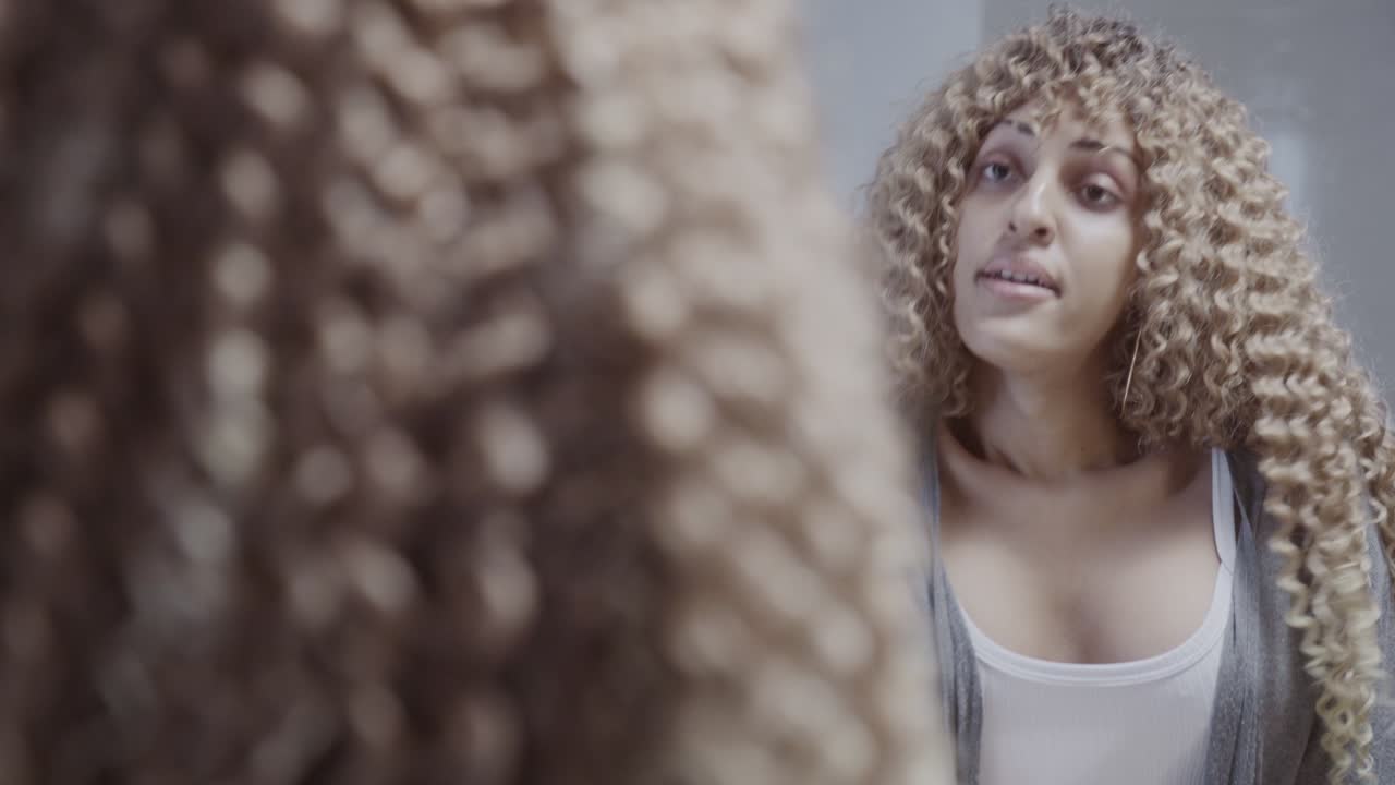 Woman with curly hair in a bathroom looking at her reflection and adjusting her clothes