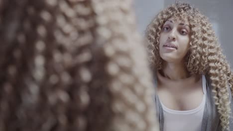 woman with curly hair in a bathroom looking at her reflection and adjusting her clothes