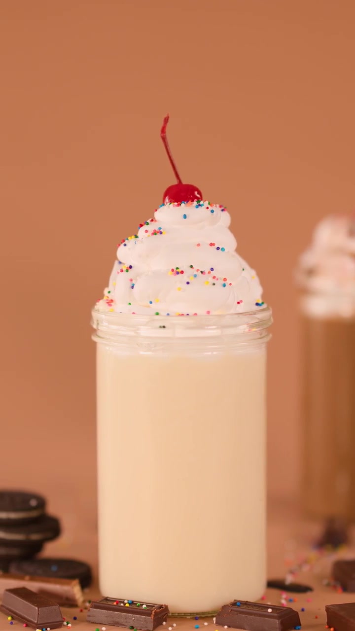 Primo piano di un milkshake alla vaniglia con panna montata e ciliegia, illuminazione calda da studio, telecamera statica