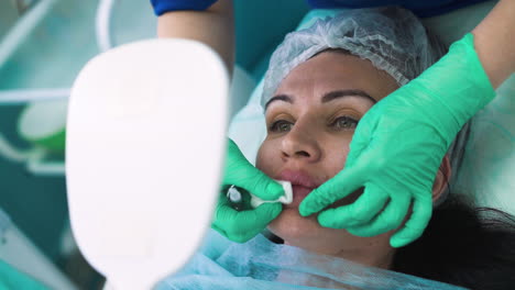 client looks into mirror while cosmetologist massages lip