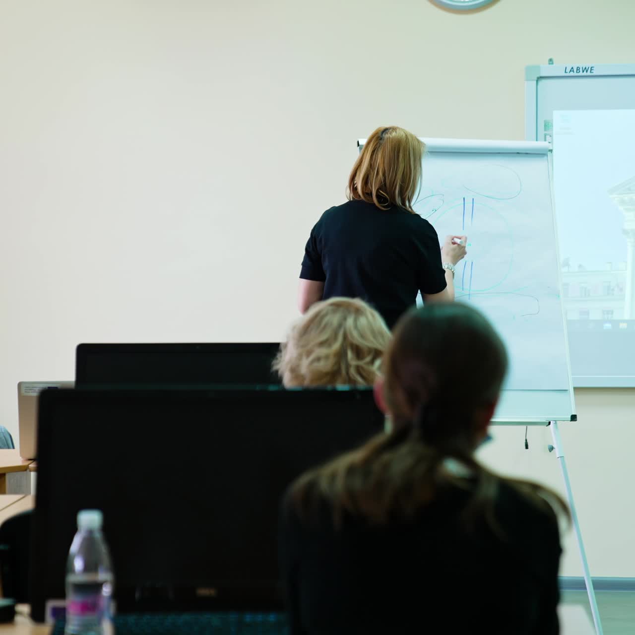 Students look at the lecturer drawing a scheme at the blackboard. Female teacher at mask explaining the eyeball structure