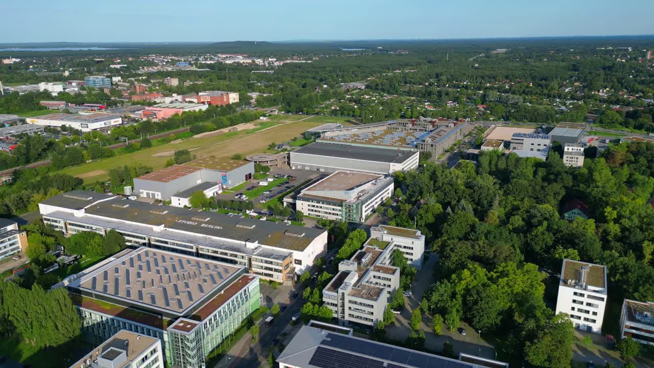 Modern film studios with offices and sound stages surrounded by trees in Berlin Adlershof, Germany. Perfect aerial view flight speed ramp hyper motion time lapse fly push forward drone