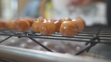 donut holes drip fresh glaze on cooling rack, closeup with soft focus background