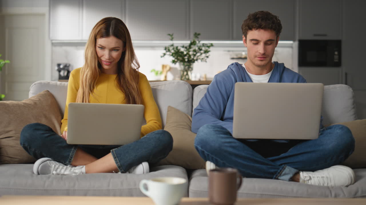 Focused lovers texting computers at couch together. Freelancers working remotely