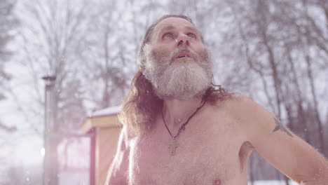 Hero shot of hippy man bare chested outdoors looking up in snowfall in prayer
