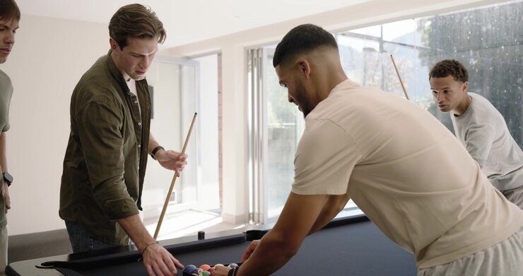 Diverse male friends placing triangular rack on black felt pool table, chatting, preparing break