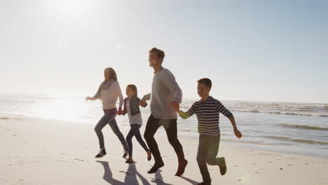 Familia-En-La-Playa-De-Invierno-Tomados-De-La-Mano-Y-Corriendo-Hacia-La-Cámara