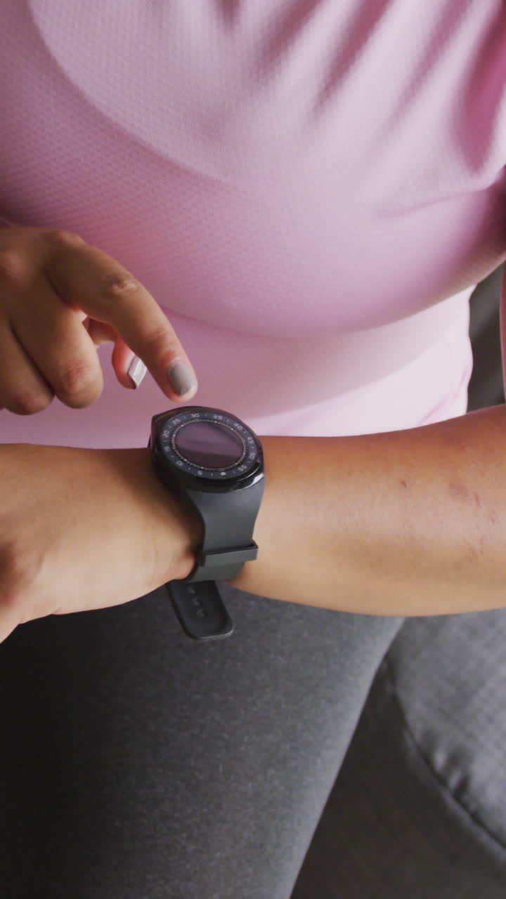 Video of midsection of plus size african american woman in sport clothes checking smartwatch