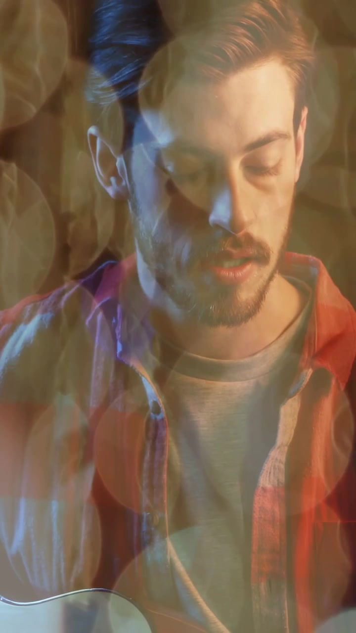 Uomo che strimpella una chitarra acustica, che canta per fare pratica musicale, con apertura della telecamera ed effetto bokeh che fluttua intorno.
