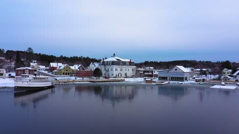 Luftaufnahmen,-Die-Im-Tiefflug-über-Eine-Dünne-Eisschicht-An-Der-Ostbucht-Des-Moosehead-Lake-In-Richtung-Der-Schneebedeckten-Innenstadt-Von-Greenville,-Maine,-Fliegen