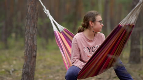 teenage girl relaxing in hammock under trees. female teen resting in weekend