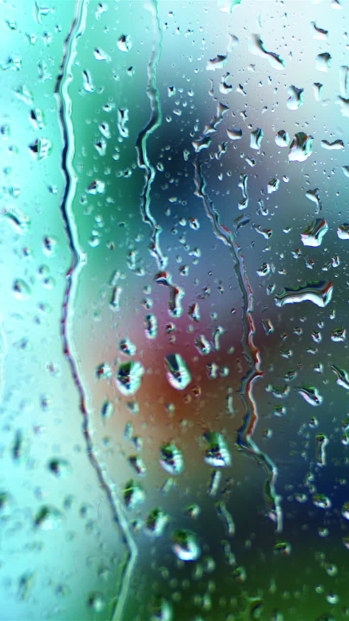 Wet window with raindrops. Water drops moving down on glass window on blur view background. Close-up. Vertical video