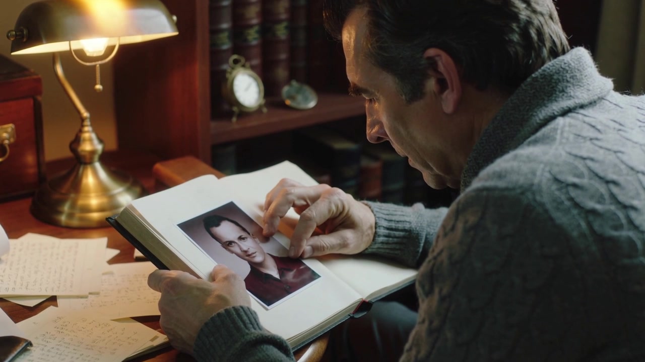 Opening album, man in grey sweater leaning by brass lamp, peeling corner inspecting portrait