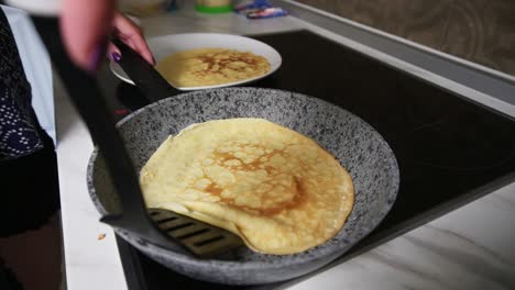 close up view of a female hand with spatula taking a prepared pancake from the pan and putting it to the plate. homemade pancakes