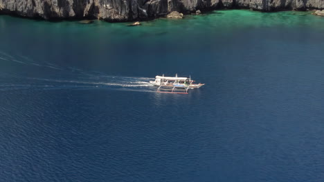 Cinematic-aerial-footage-of-an-outrigger-boat-driving-by-the-cliffs-in-Palawan,-Philippines,-Asia,-Drone