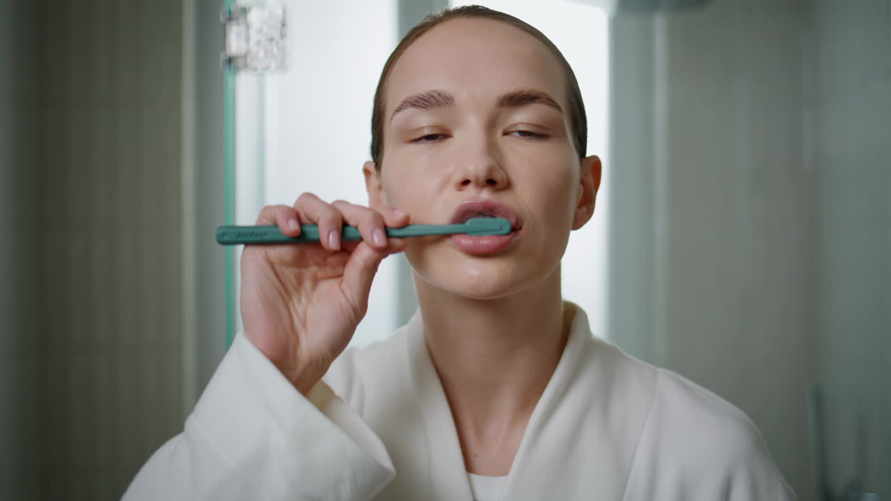 Home girl brushing teeth in morning bathroom. Closeup calm woman looking camera