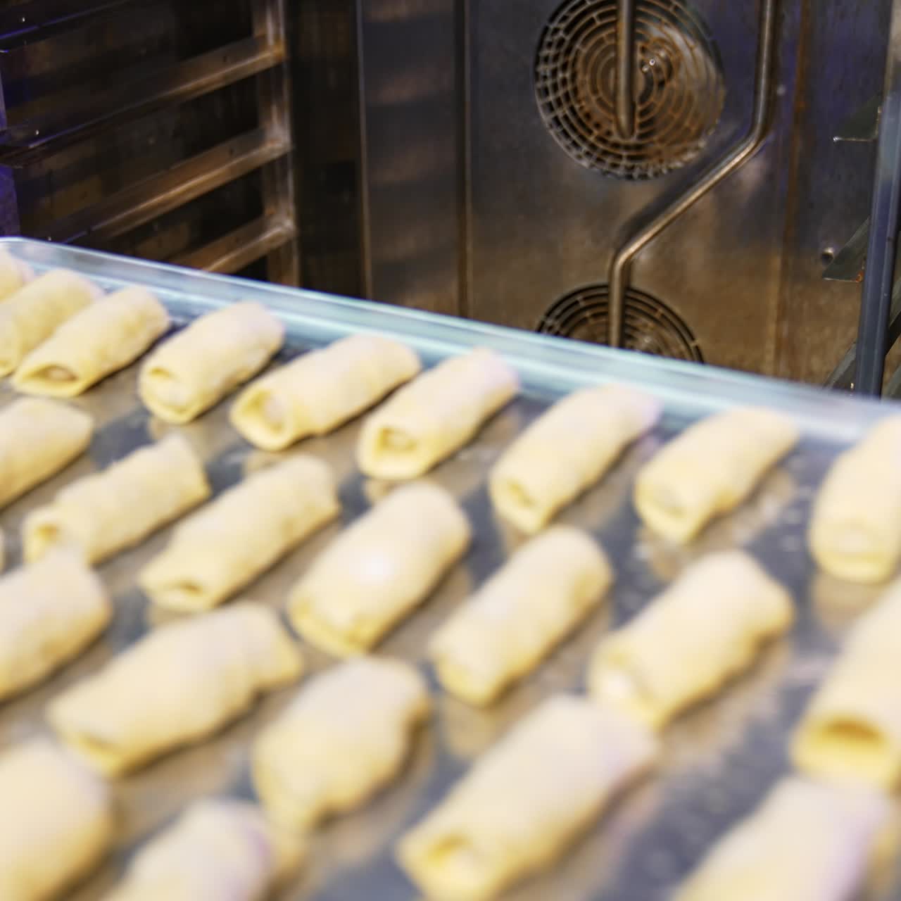 Baker puts three baking sheets filled with little croissants into the oven. Sweet pastry production at modern bakery