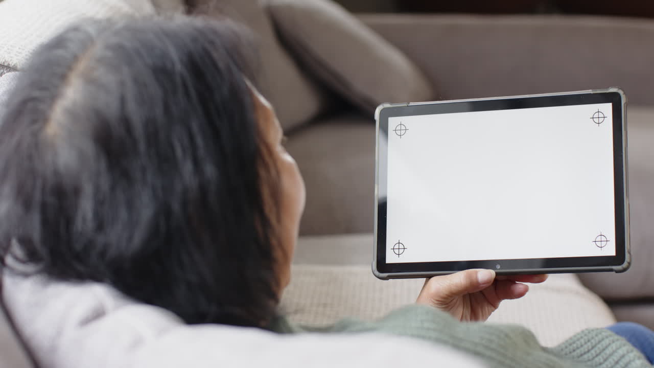 Senior woman relaxing on couch holding tablet with blank screen at home, copy space
