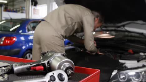 mecánico usando una computadora portátil mientras hace servicio a un motor de automóvil